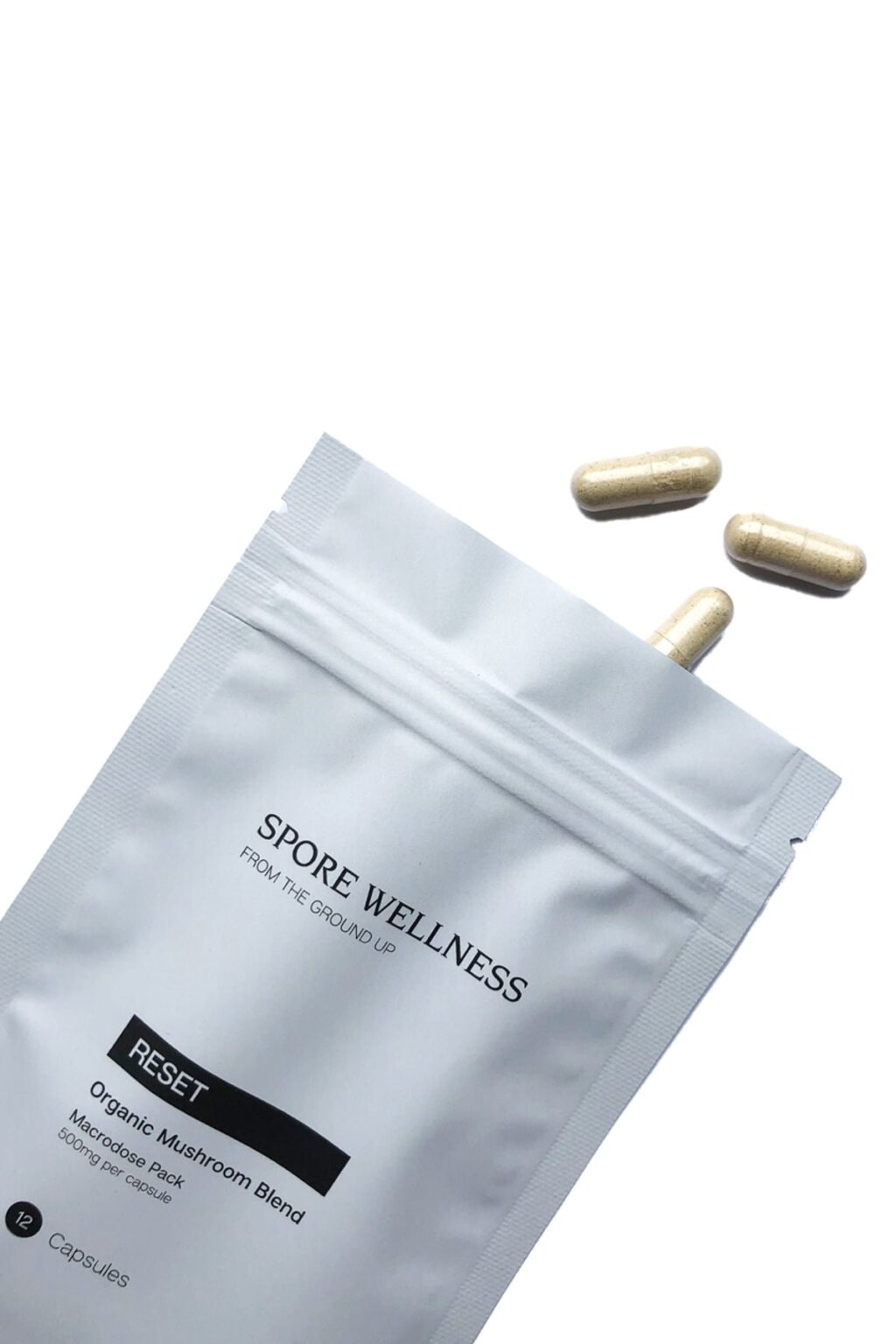 Spore Wellness brand Reset container standing next to several two piece vegetable capsules